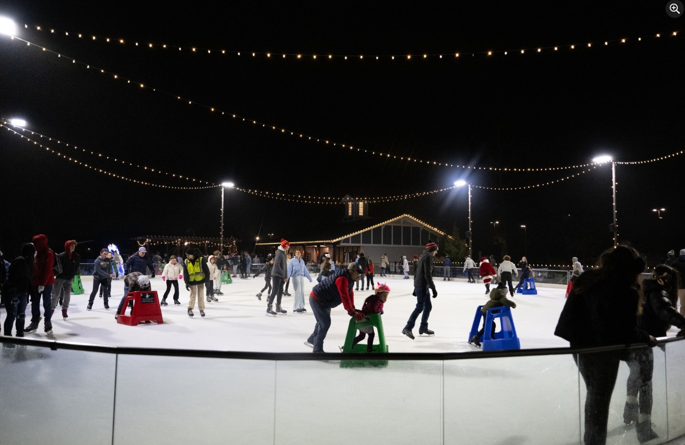 ice skating rink full of adults and children ice skating at night time